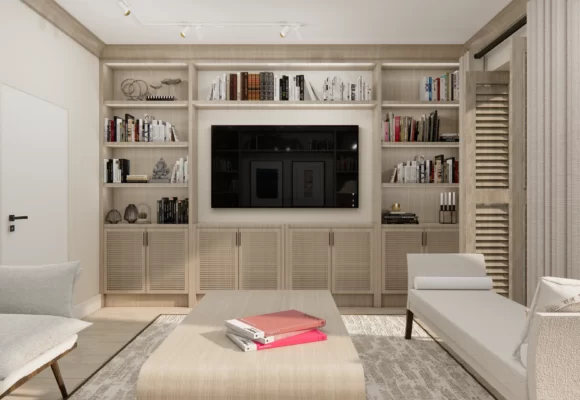Wnętrze cechuje się jasną, neutralną kolorystyką, która nadaje przestrzeni lekkości i optycznie ją powiększa. W centrum znajduje się zabudowa z półkami, które są ozdobione książkami oraz dekoracjami, dodającymi wnętrzu osobistego charakteru. Telewizor został wkomponowany w środek zabudowy, tworząc funkcjonalną i estetyczną przestrzeń. Całość dopełniają proste, ale stylowe meble – jasne fotele i stolik kawowy, na którym spoczywają książki i magazyny w wyrazistych kolorach.